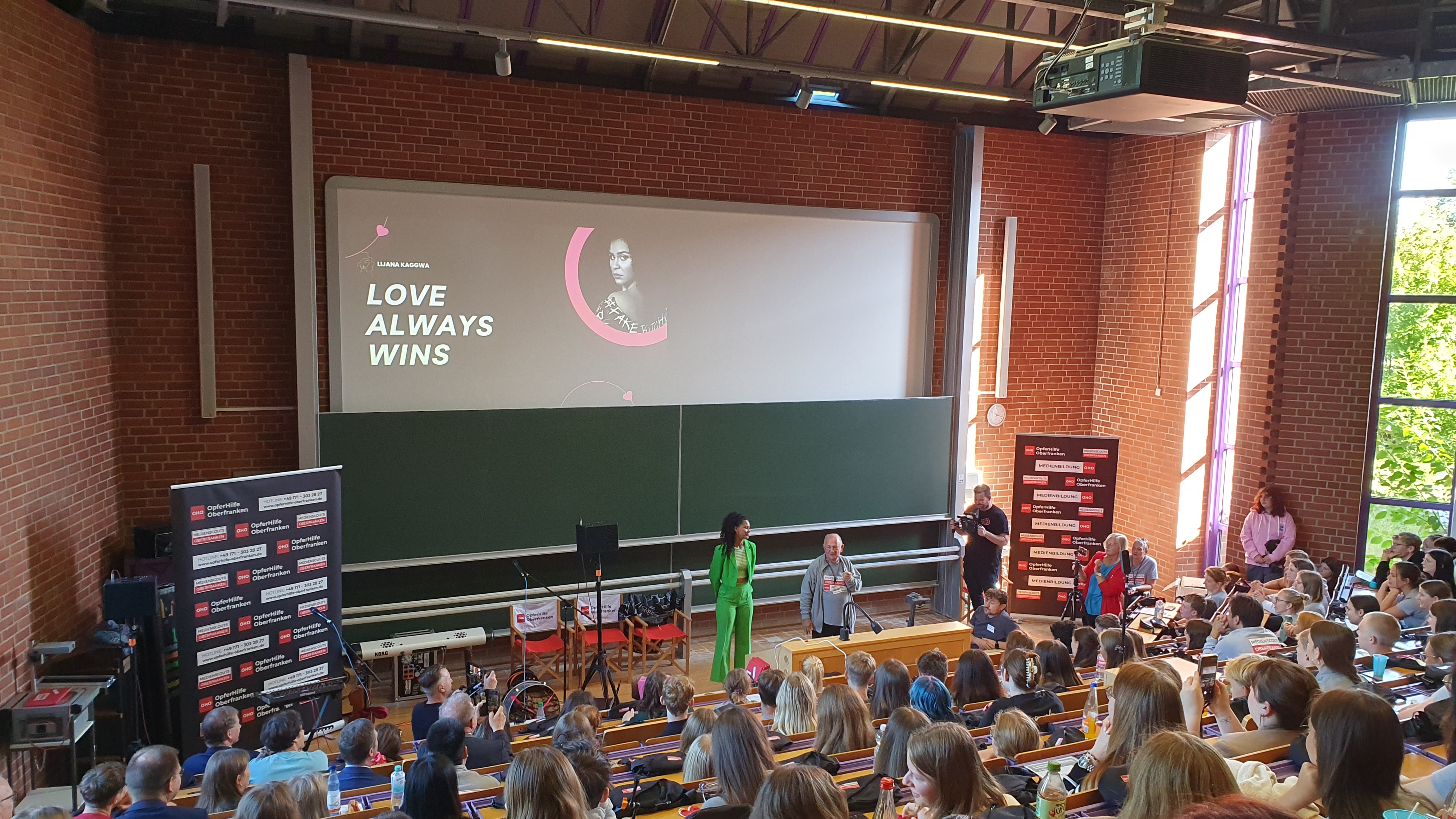 Ausbildungstag Medienscouts in Bayreuth - Foto in einem Hörsaal mit Lijana Kaggwa, Alfons Hrubesch und den über 300 Schülerinnen und Schülern